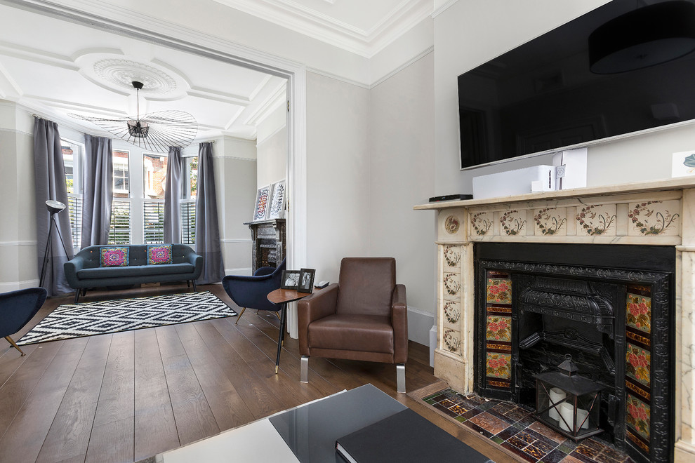Пример оригинального дизайна: гостиная комната в стиле неоклассика (современная классика) с стандартным камином, фасадом камина из камня, телевизором на стене и коричневым полом