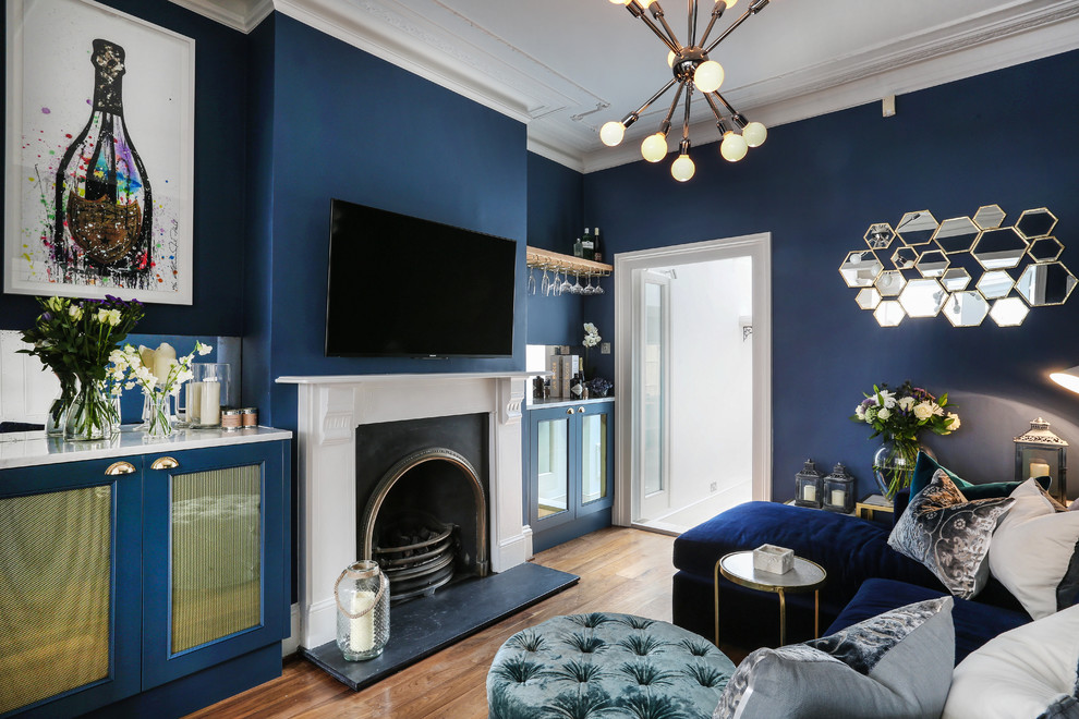 Modelo de sala de estar con barra de bar cerrada, ecléctica, con paredes azules, suelo de madera en tonos medios, todas las chimeneas y televisor colgado en la pared