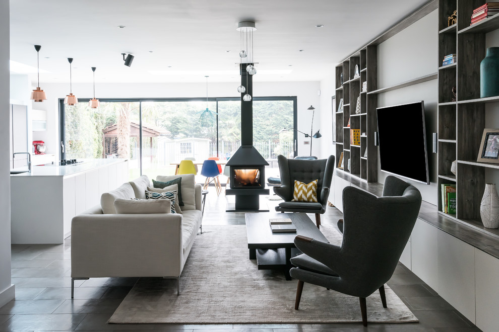 Modelo de sala de estar abierta contemporánea con paredes blancas, estufa de leña, televisor colgado en la pared y suelo gris