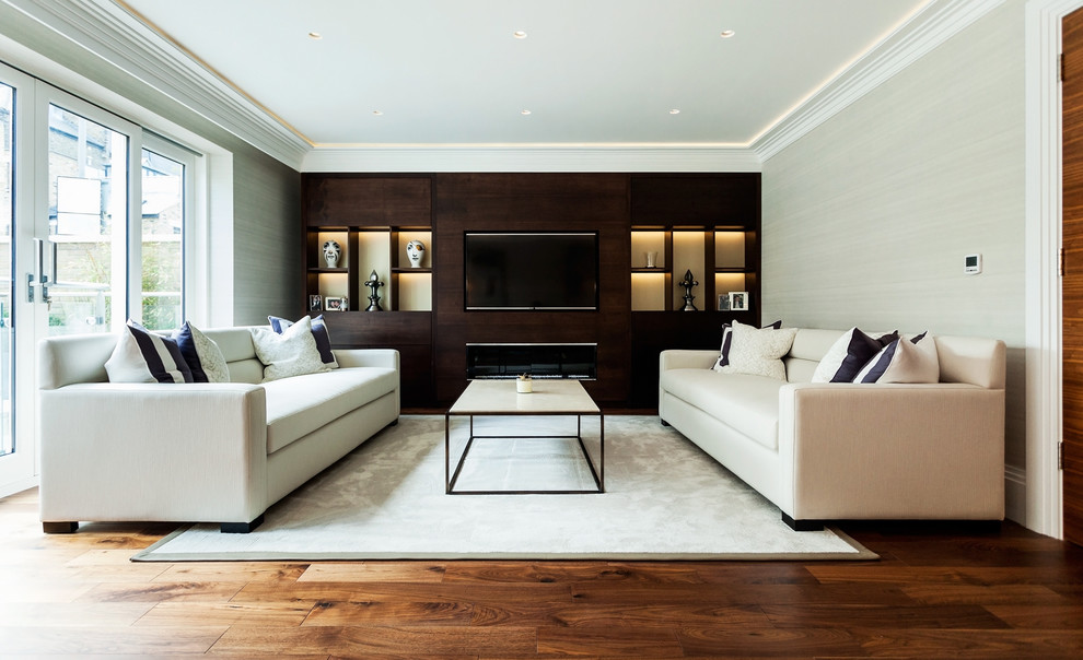 Aménagement d'une salle de séjour contemporaine avec un mur beige, un sol en bois brun, une cheminée ribbon et un téléviseur encastré.