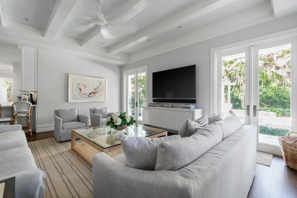 Imagen de sala de estar costera con paredes grises, suelo de madera oscura, televisor colgado en la pared, suelo marrón y vigas vistas