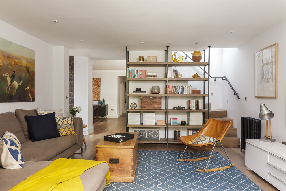 Modelo de sala de estar con biblioteca bohemia sin chimenea con paredes blancas y suelo de madera en tonos medios