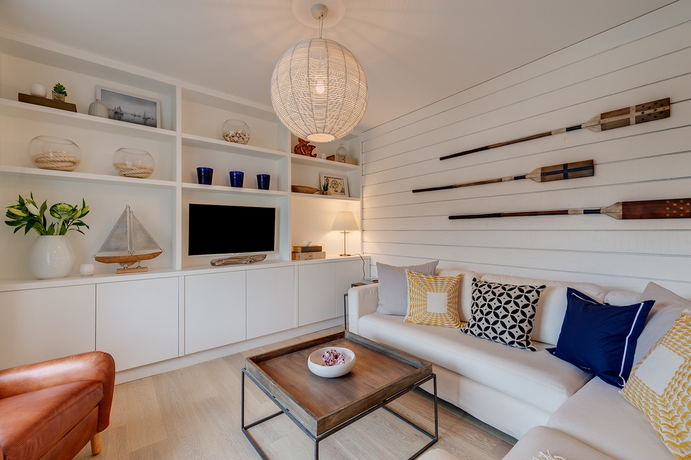 Imagen de sala de estar abierta marinera sin chimenea con paredes blancas, suelo de madera clara y pared multimedia