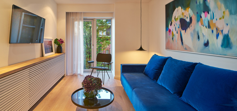Imagen de sala de estar cerrada actual de tamaño medio con paredes blancas, suelo de madera clara y televisor colgado en la pared