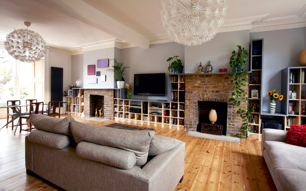 Immagine di un soggiorno classico aperto con pareti blu, parquet chiaro, cornice del camino in mattoni, TV a parete, libreria e camino classico