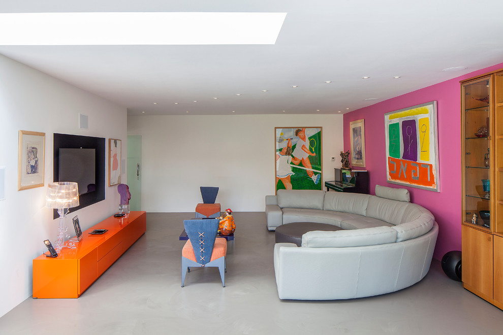 Modelo de sala de estar cerrada contemporánea grande sin chimenea con suelo de cemento, televisor colgado en la pared y paredes multicolor