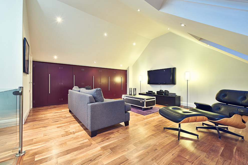 This is an example of a large contemporary open plan games room in London with white walls, medium hardwood flooring and a wall mounted tv.