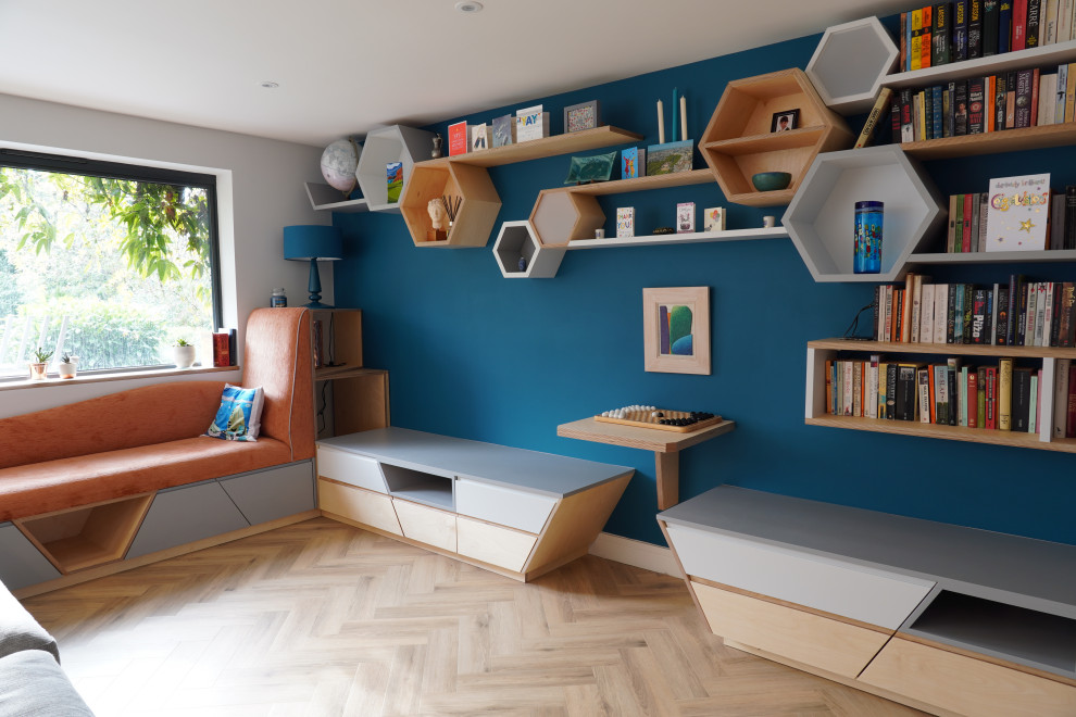На фото: открытая гостиная комната среднего размера в скандинавском стиле с с книжными шкафами и полками, синими стенами, паркетным полом среднего тона и коричневым полом с