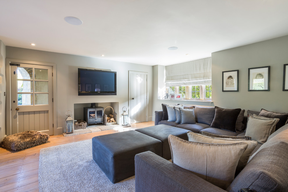 Abgetrenntes, Mittelgroßes Landhaus Wohnzimmer mit grauer Wandfarbe, TV-Wand, Kaminofen, braunem Holzboden und beigem Boden in Gloucestershire