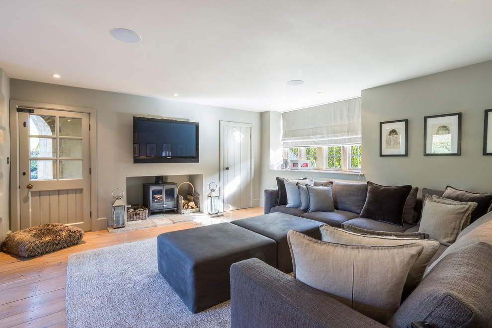 This is an example of a medium sized rural enclosed games room in Gloucestershire with grey walls, a wall mounted tv, a wood burning stove, medium hardwood flooring and beige floors.