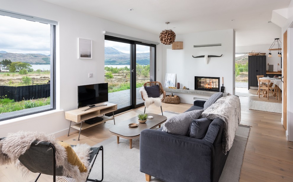 Diseño de sala de estar escandinava de tamaño medio con paredes blancas, suelo de madera clara, chimenea de doble cara, televisor independiente y suelo beige
