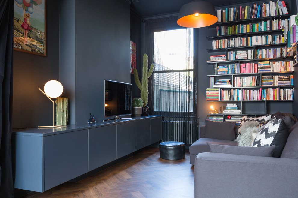 Modelo de sala de estar con biblioteca abierta contemporánea de tamaño medio con paredes negras, suelo de madera oscura y televisor independiente