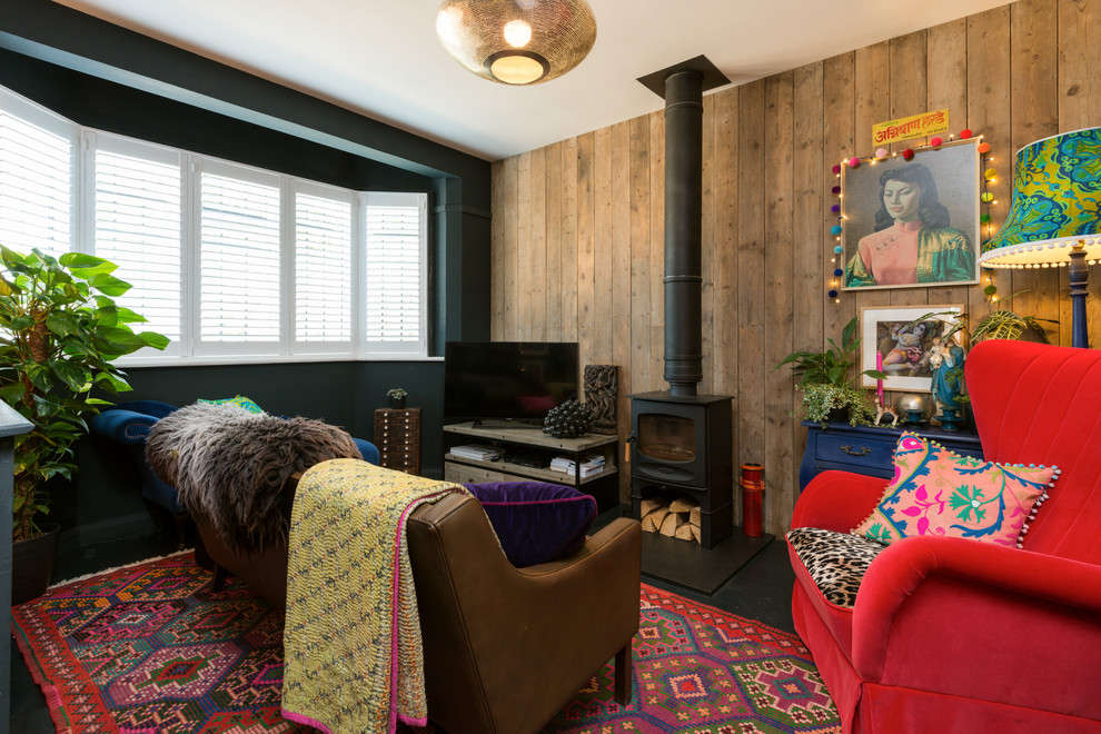 Стильный дизайн: гостиная комната среднего размера в стиле фьюжн с печью-буржуйкой, отдельно стоящим телевизором и черными стенами - последний тренд