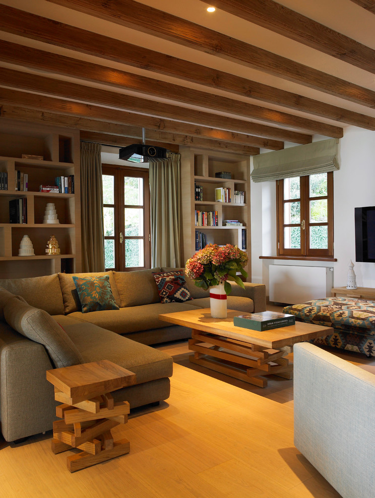 Imagen de sala de estar mediterránea grande con paredes blancas, suelo de madera clara y televisor colgado en la pared