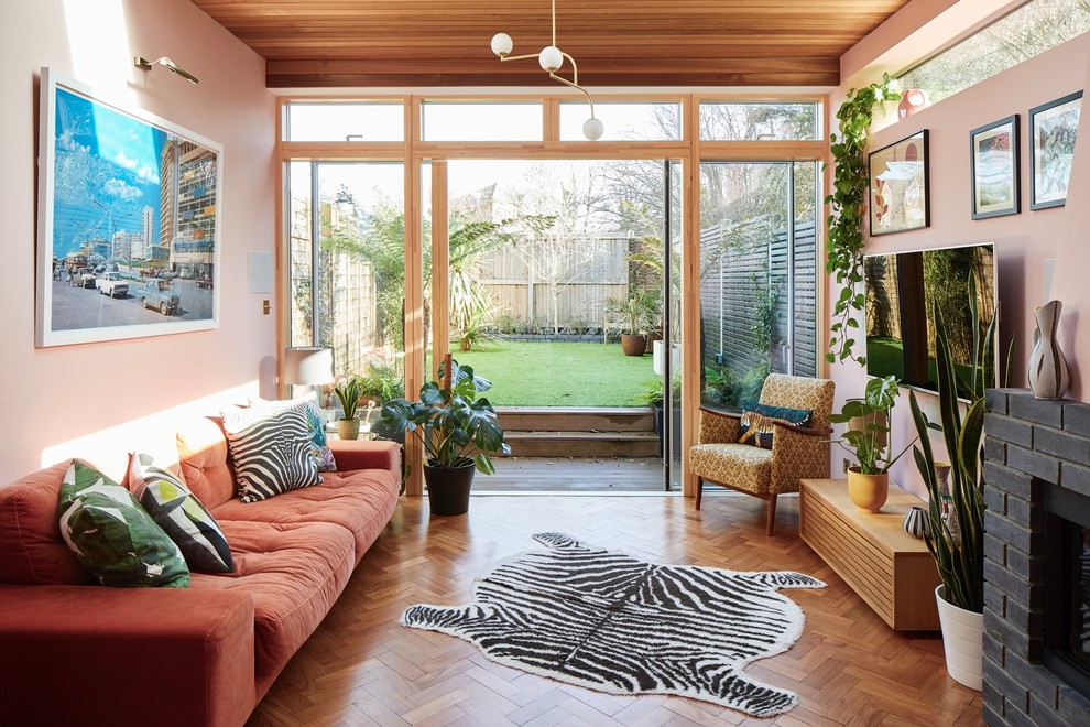 Foto di un soggiorno minimalista con pareti rosa, pavimento in legno massello medio, cornice del camino in mattoni e TV a parete