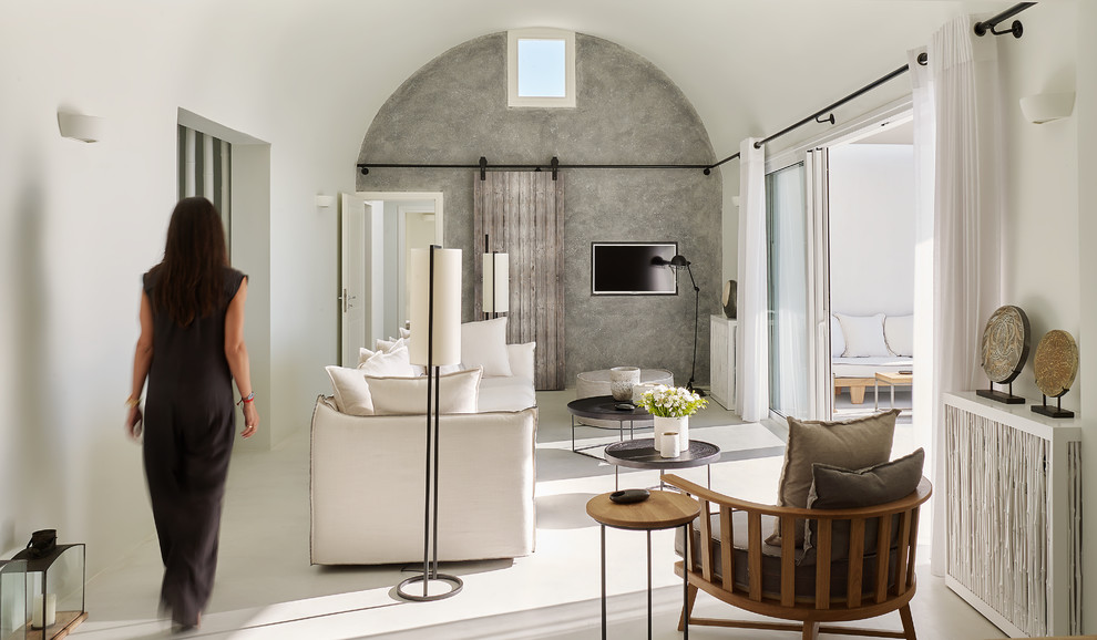 На фото: гостиная комната в средиземноморском стиле с серыми стенами, телевизором на стене и белым полом без камина
