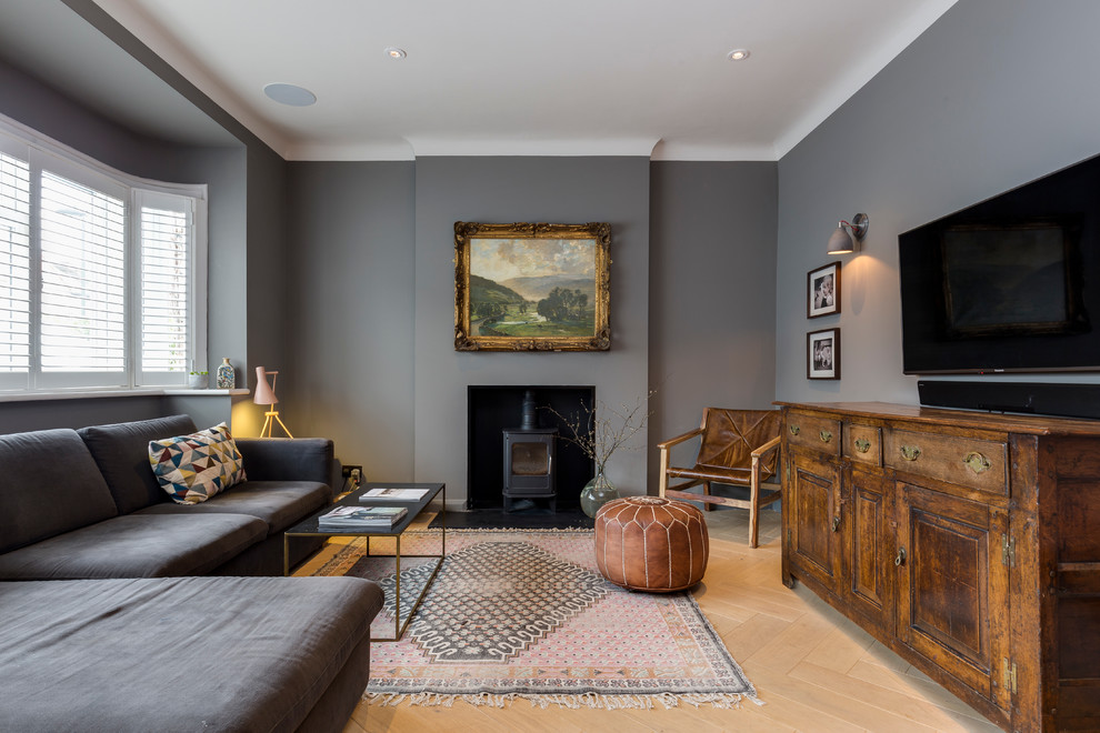 На фото: гостиная комната в стиле неоклассика (современная классика) с серыми стенами, светлым паркетным полом, стандартным камином, телевизором на стене и ковром на полу с