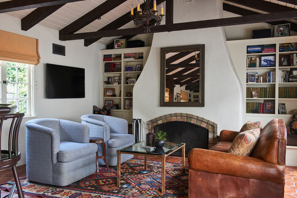 This is an example of a medium sized mediterranean enclosed games room in Los Angeles with a home bar, white walls, terracotta flooring, a standard fireplace, a tiled fireplace surround, a wall mounted tv and orange floors.