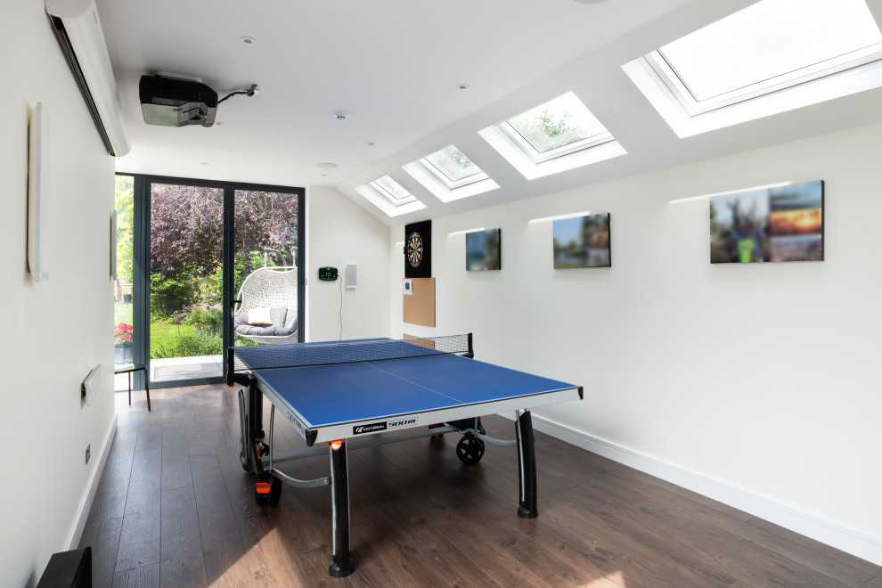 Inspiration for a mid-sized modern enclosed medium tone wood floor and brown floor game room remodel in Surrey with white walls