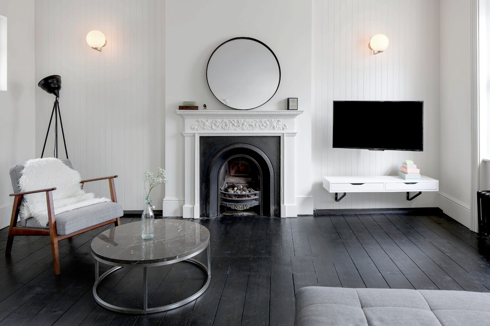 Imagen de sala de estar abierta actual de tamaño medio con paredes blancas, suelo de madera oscura, todas las chimeneas, marco de chimenea de yeso, televisor colgado en la pared y suelo negro