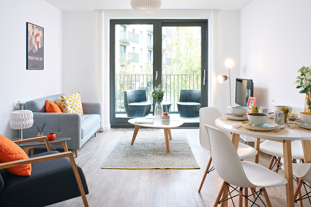 Стильный дизайн: открытая гостиная комната в скандинавском стиле с белыми стенами, светлым паркетным полом и отдельно стоящим телевизором без камина - последний тренд