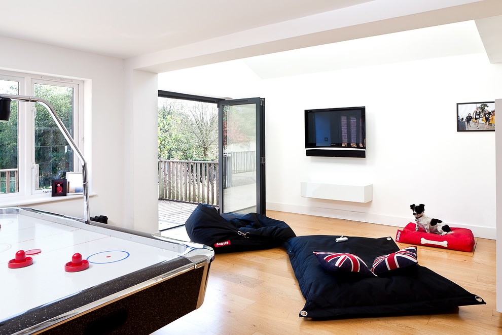 Esempio di un soggiorno design con sala giochi, pareti bianche, parquet chiaro e TV a parete