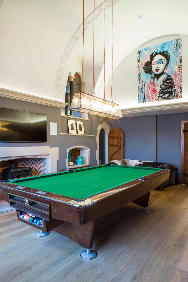 Photo of a large traditional enclosed games room in Oxfordshire with light hardwood flooring, a wood burning stove, a wall mounted tv and brown floors.