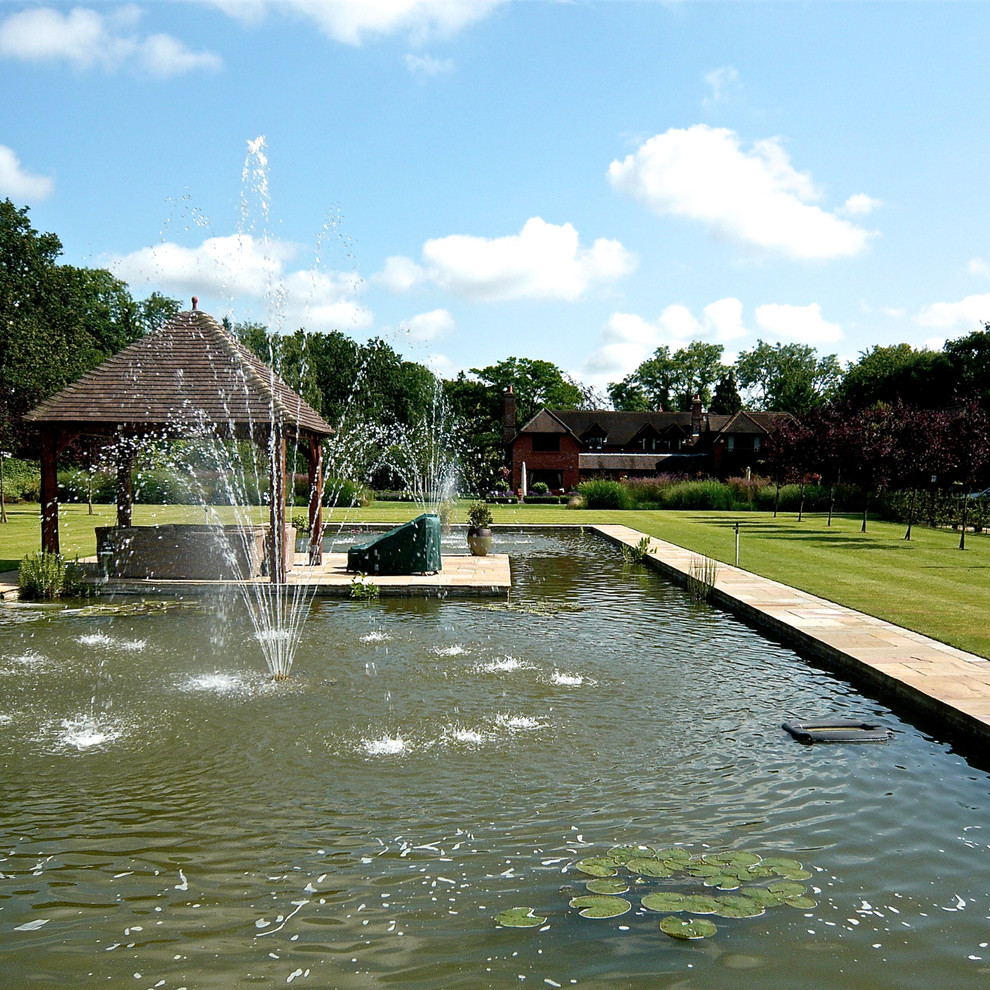 Foto di un ampio giardino country esposto in pieno sole dietro casa con fontane e pavimentazioni in pietra naturale
