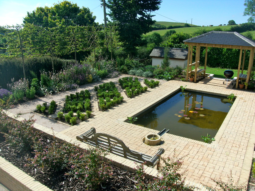 Design ideas for a medium sized mediterranean front formal full sun raised pond for summer in Devon with a water feature and brick paving.