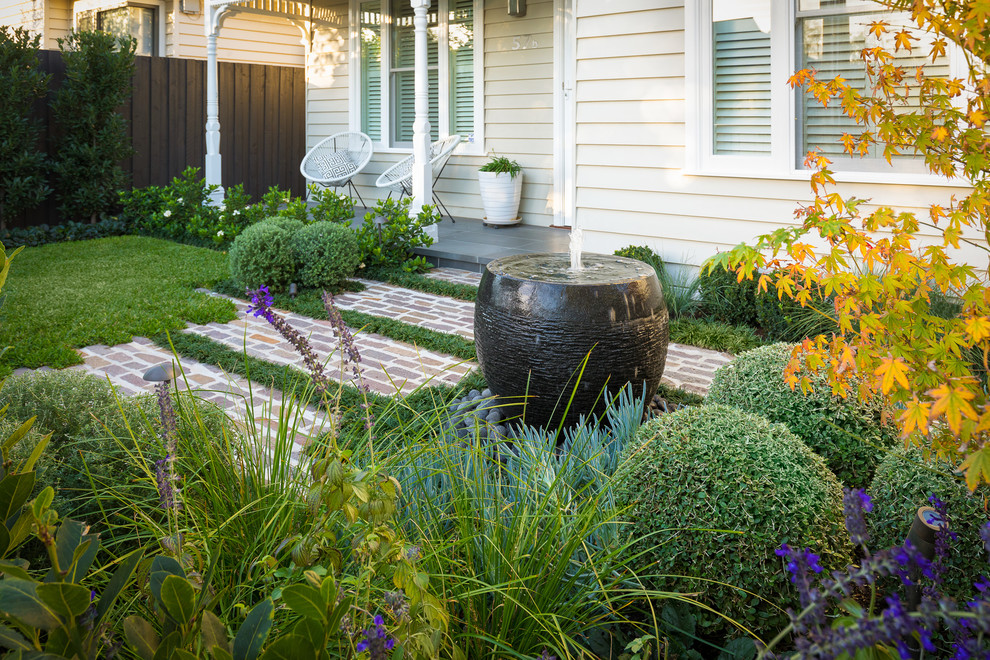 Exempel på en liten trädgård framför huset, med en fontän och naturstensplattor