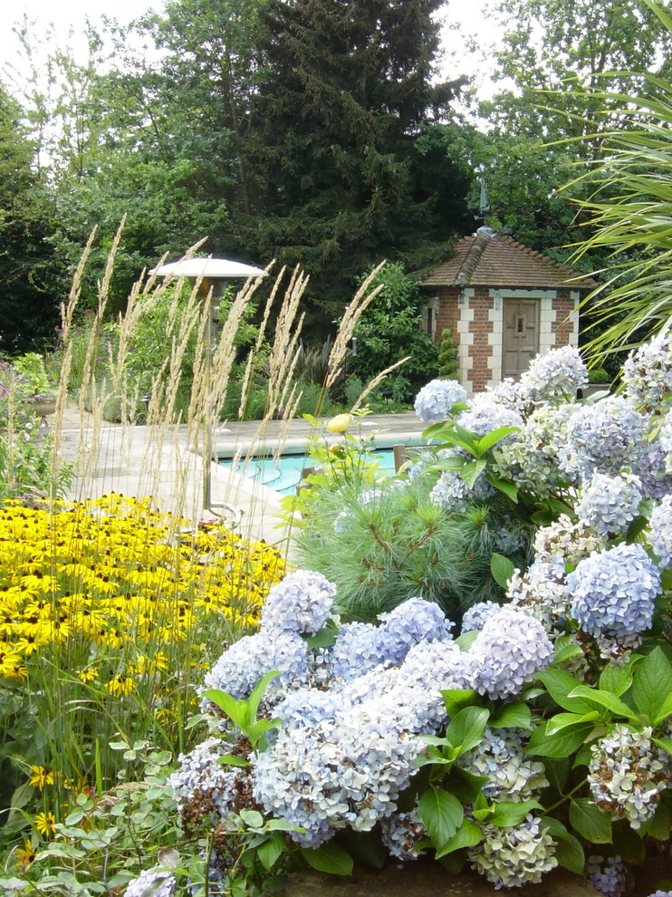 Imagen de jardín tradicional extra grande en verano en patio trasero con exposición parcial al sol y adoquines de piedra natural