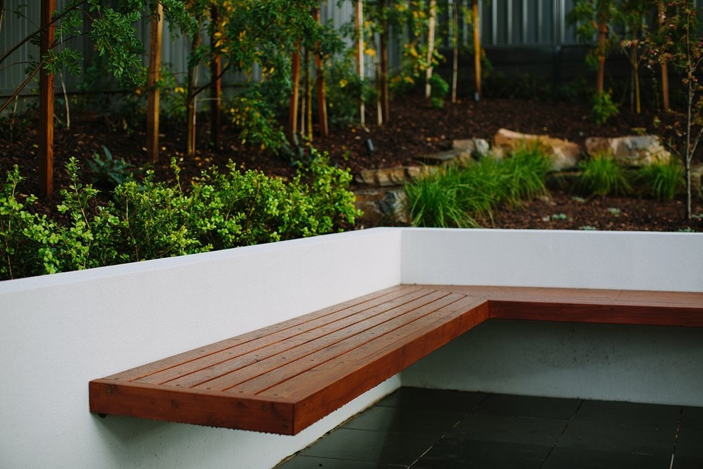 Diseño de acceso privado minimalista de tamaño medio en patio delantero con muro de contención, exposición total al sol y adoquines de piedra natural