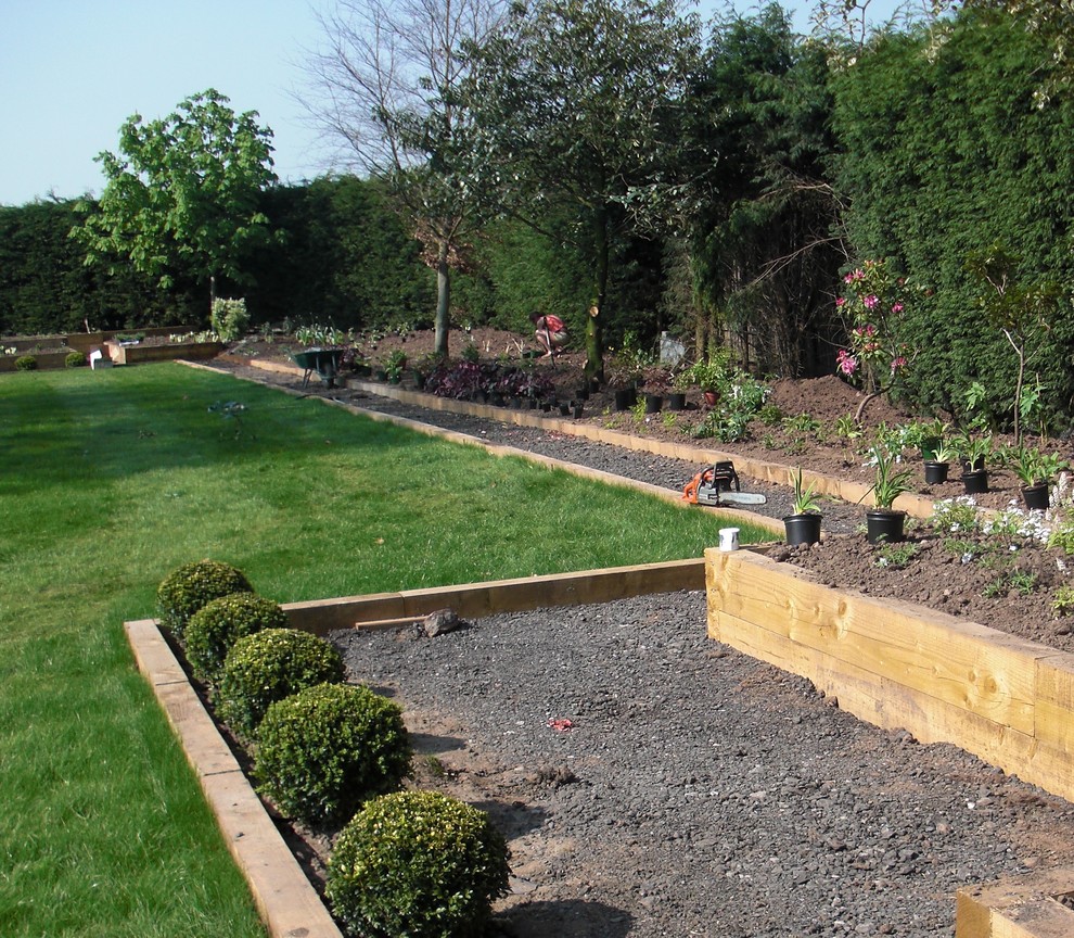 Foto på en mycket stor funkis trädgård i full sol på sommaren, med en stödmur och grus