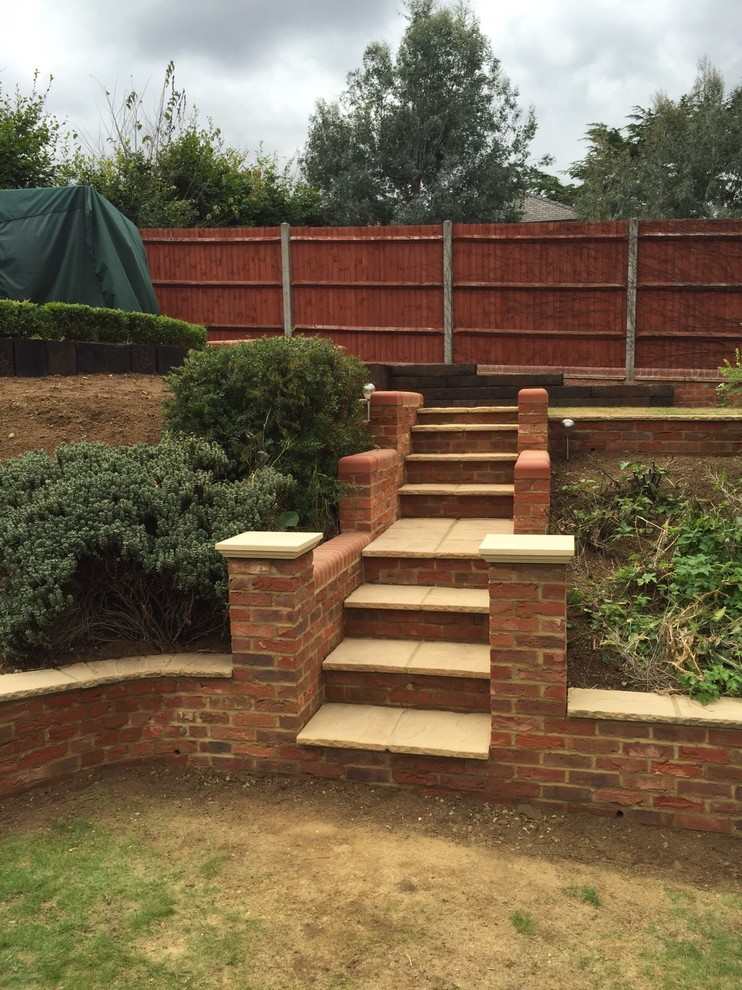 Photo of a medium sized sloped formal full sun garden for spring in Other with a retaining wall and brick paving.