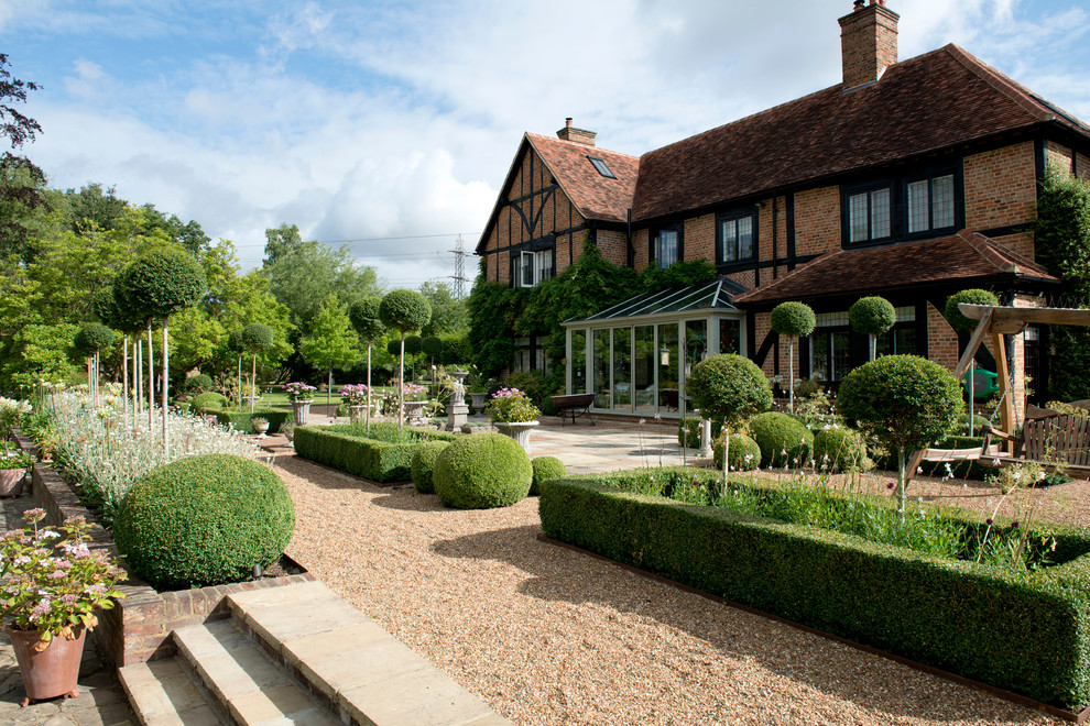 Immagine di un ampio giardino formale tradizionale esposto in pieno sole dietro casa in estate con ghiaia