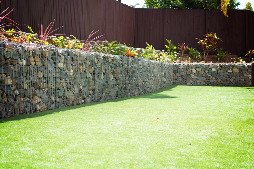 Photo of a mid-sized modern partial sun backyard retaining wall landscape in Brisbane.