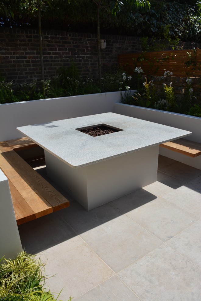 This is an example of a small contemporary back full sun garden in London with a fire feature and natural stone paving.