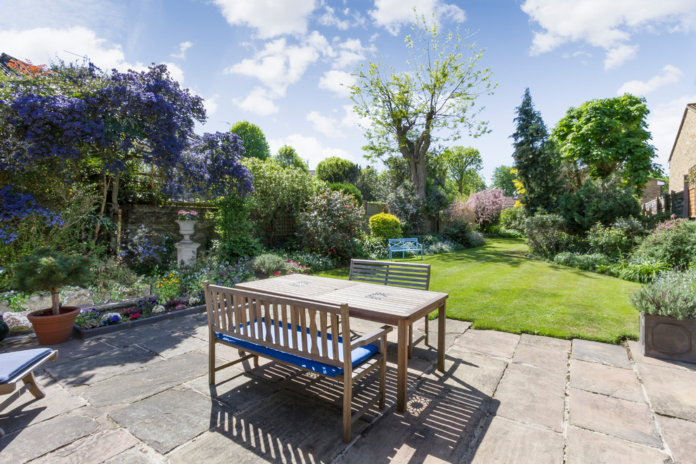 This is an example of an expansive traditional back garden seating in London with natural stone paving.