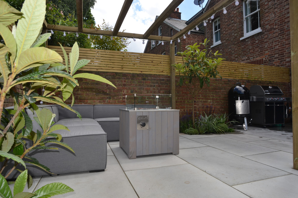 This is an example of a small contemporary back partial sun garden in Sussex with a fire feature and natural stone paving.