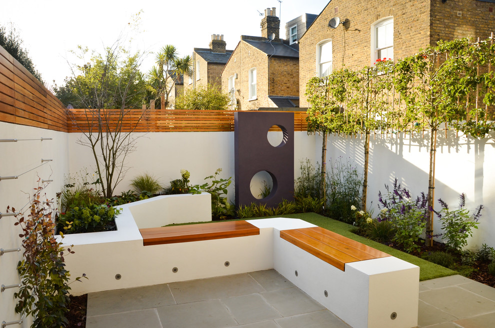 This is an example of a small contemporary back partial sun garden for summer in London with natural stone paving.