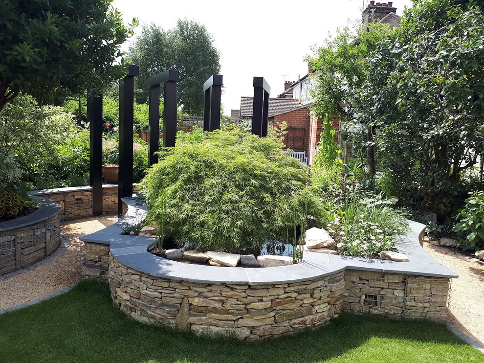 Inspiration for a medium sized modern back full sun raised pond for autumn in Hertfordshire with a retaining wall and natural stone paving.