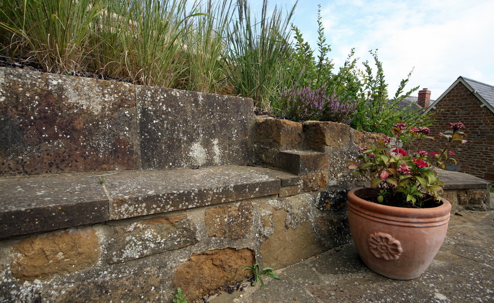Aménagement d'un grand jardin à la française campagne l'été avec un mur de soutènement, une exposition ensoleillée, une pente, une colline ou un talus et des pavés en pierre naturelle.