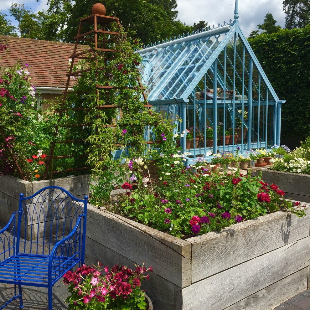 Modelo de jardín tradicional grande en verano en patio trasero con jardín francés, macetero elevado, exposición total al sol y adoquines de ladrillo