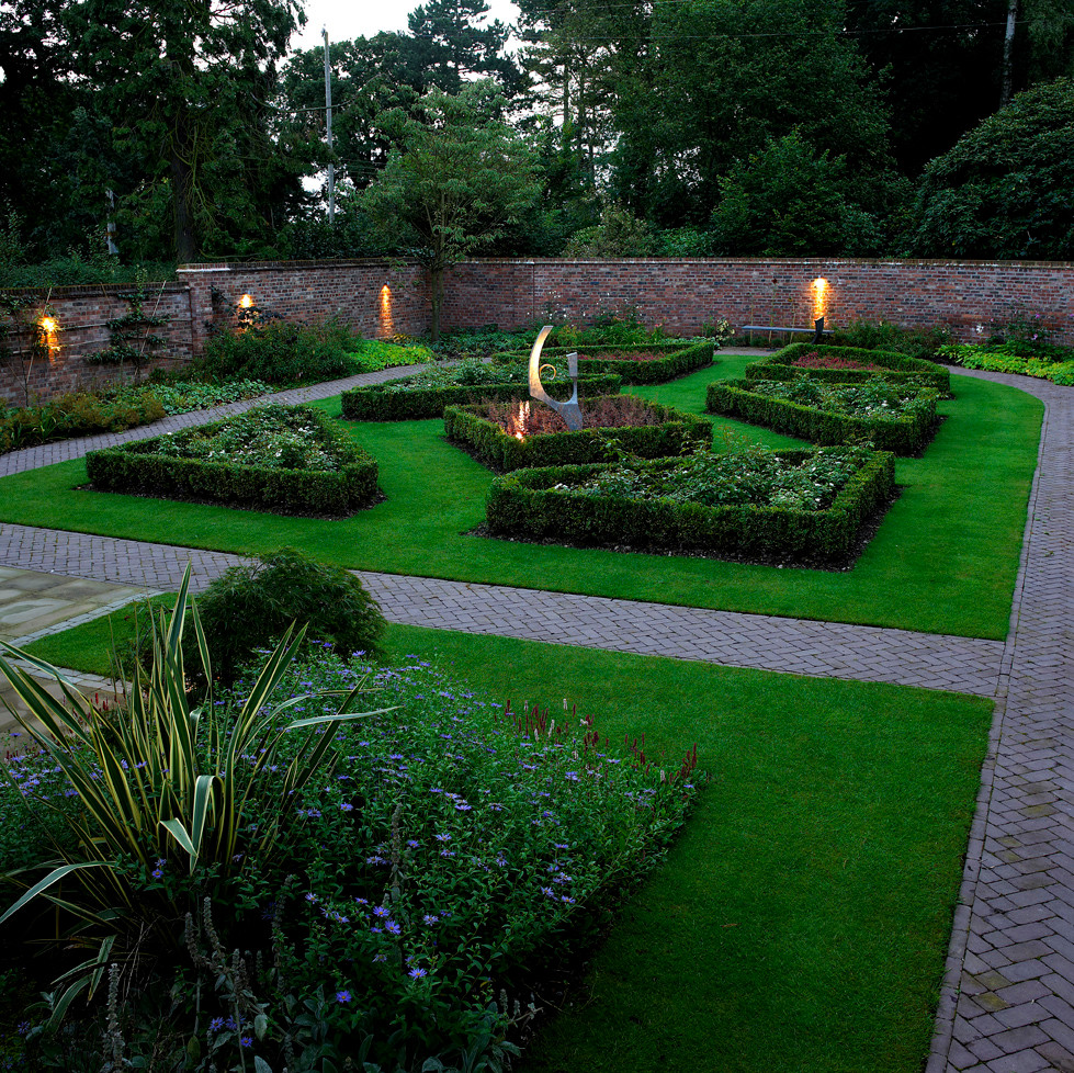 Идея дизайна: большой регулярный сад на внутреннем дворе с подпорной стенкой, полуденной тенью и мощением тротуарной плиткой