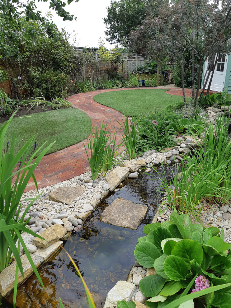 Réalisation d'un jardin arrière champêtre de taille moyenne avec un bassin et des galets de rivière.