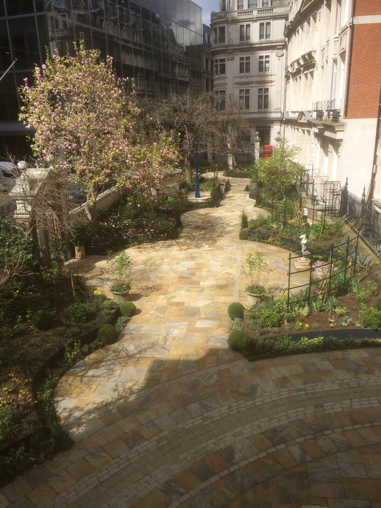 На фото: большой регулярный сад на заднем дворе в классическом стиле с полуденной тенью и покрытием из каменной брусчатки