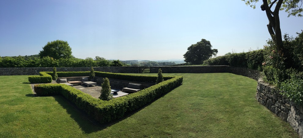 Exempel på en mycket stor klassisk trädgård i full sol på sommaren, med en stödmur och naturstensplattor