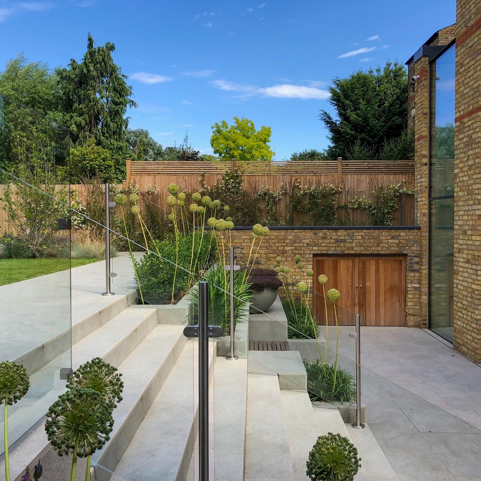 Photo of a mid-sized contemporary partial sun backyard stone landscaping in London for summer.
