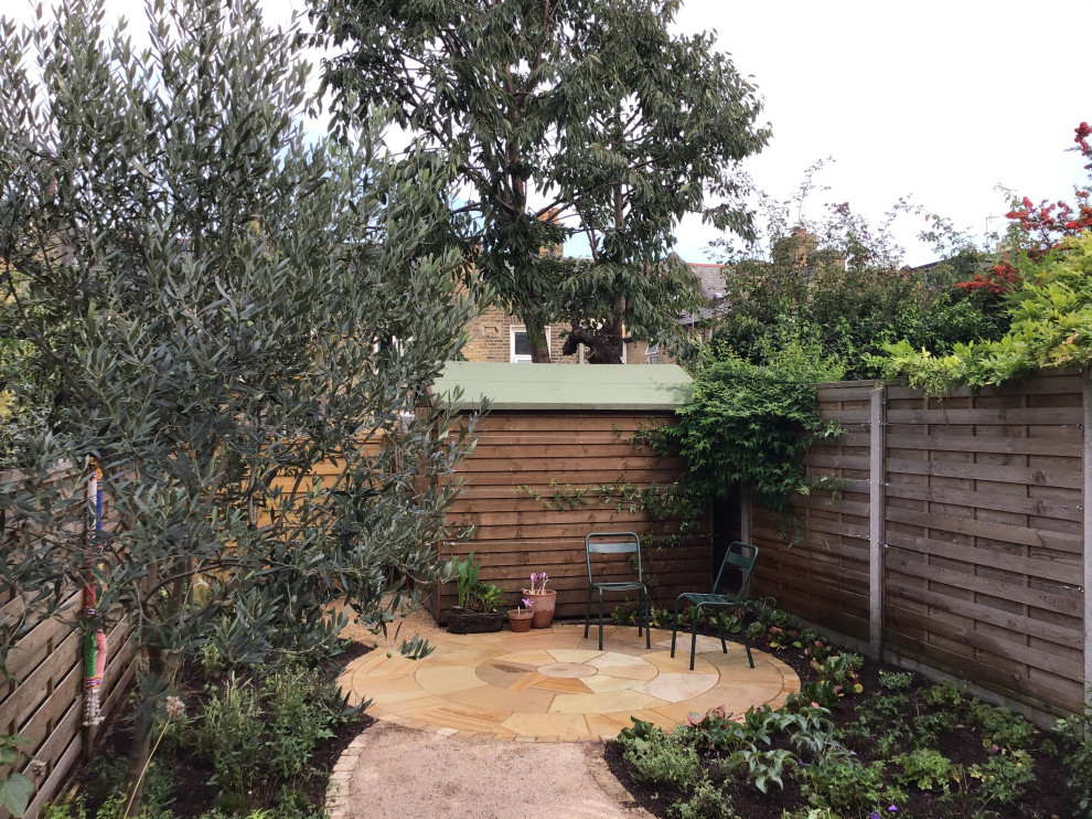 Small mediterranean back xeriscape partial sun garden for summer in London with a garden path and natural stone paving.