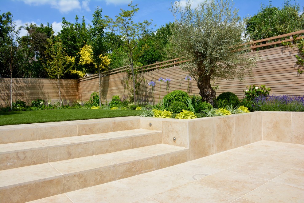 Medium sized contemporary back full sun garden for summer in London with natural stone paving.